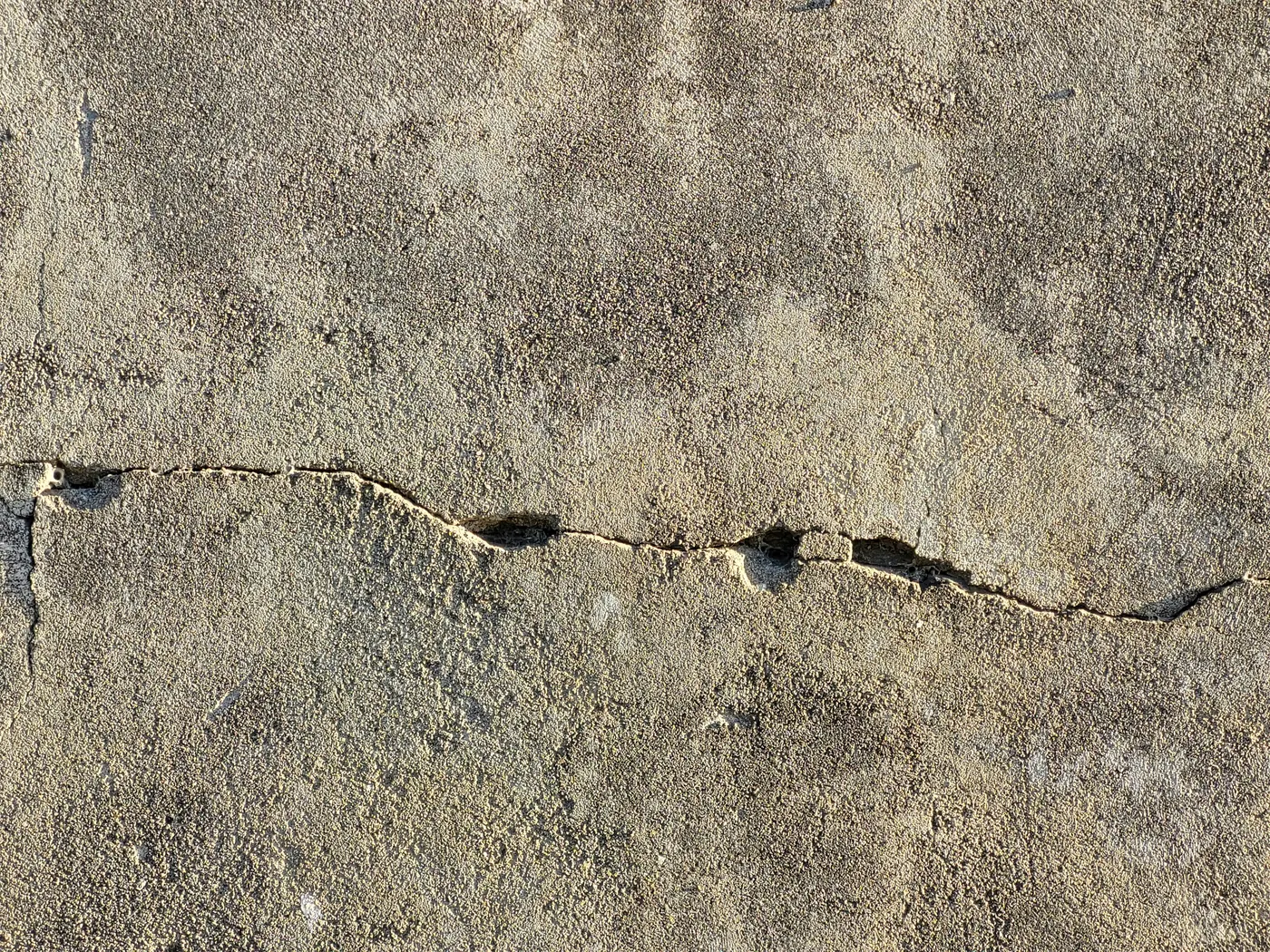 Close-up of a jagged horizontal crack across a rough cement wall surface