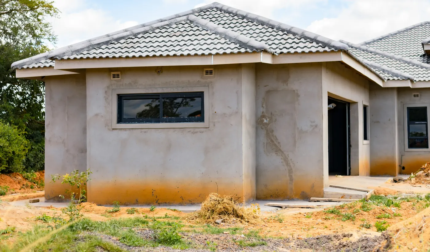 New stucco house with orange soil stains along the bottom of its walls and bare dirt around it
